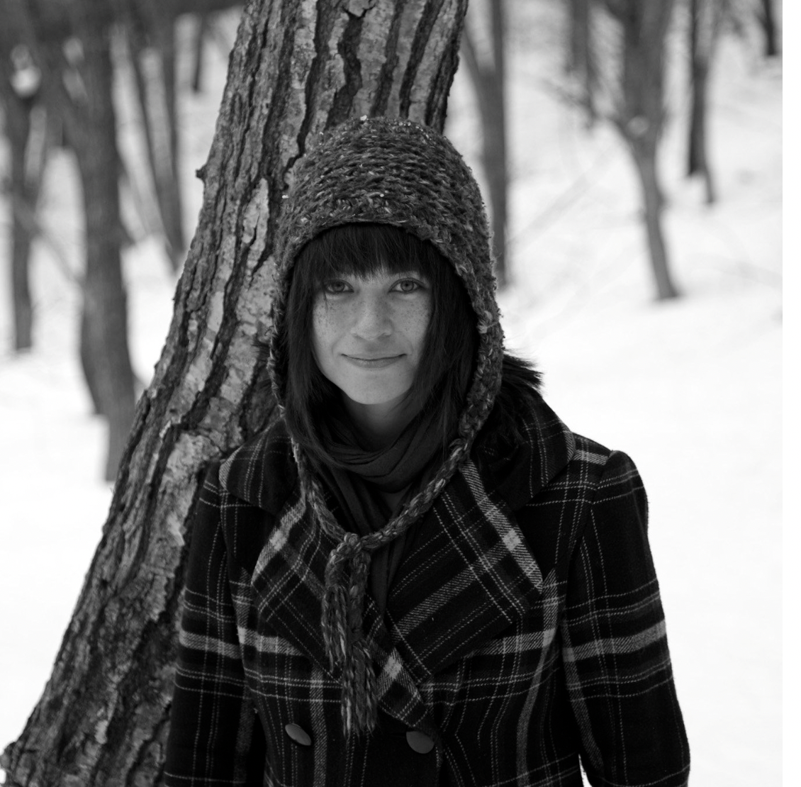 A black and white photo of Amanda wearing a beanie and plaid coat in a snowy environment.